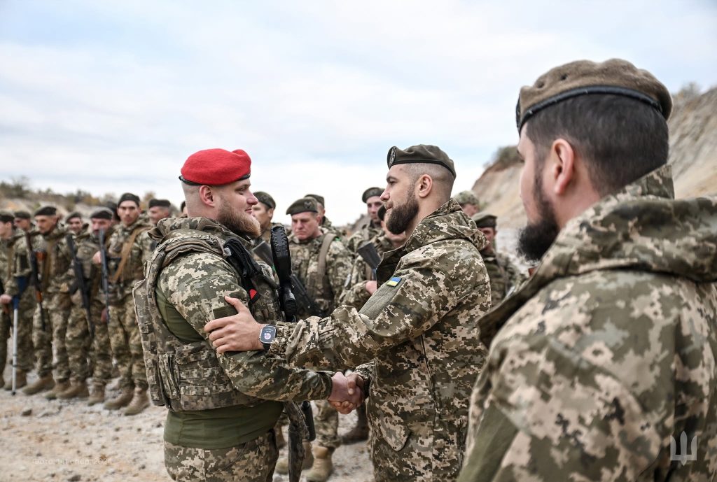 Командир у червоному береті тисне руку бійцеві перед строєм військових 141 ОМБр на відкритій місцевості