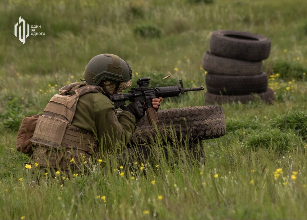 Боєць 141 ОМБр веде вогонь із гвинтівки з-за укриття з покришок під час навчань у полі